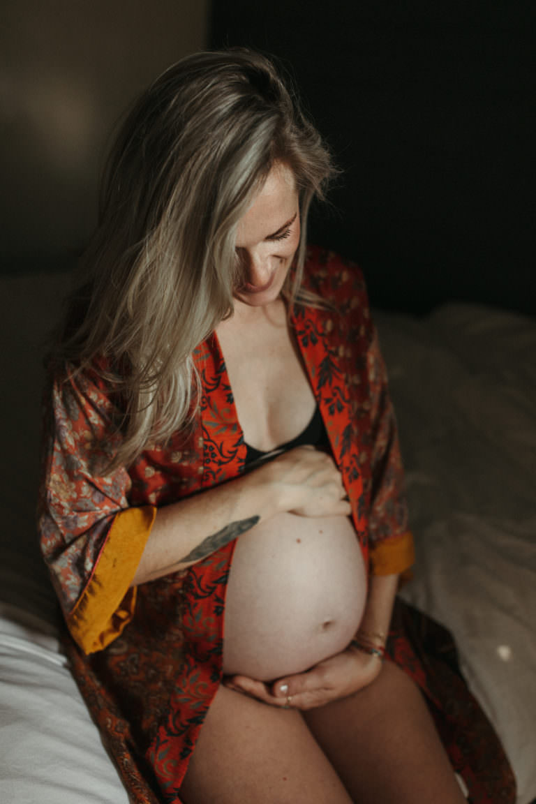 women sits holding pregnant stomach in beautiful red boho dressing gown